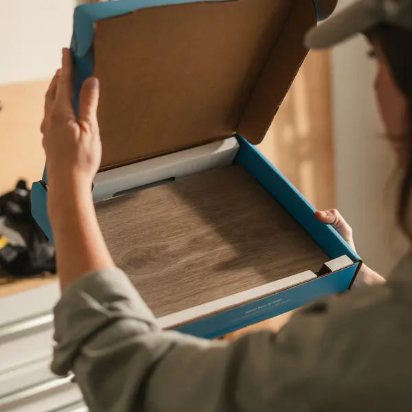 Hands lifting the lid off a Flooret sample box with a wood-look sample inside